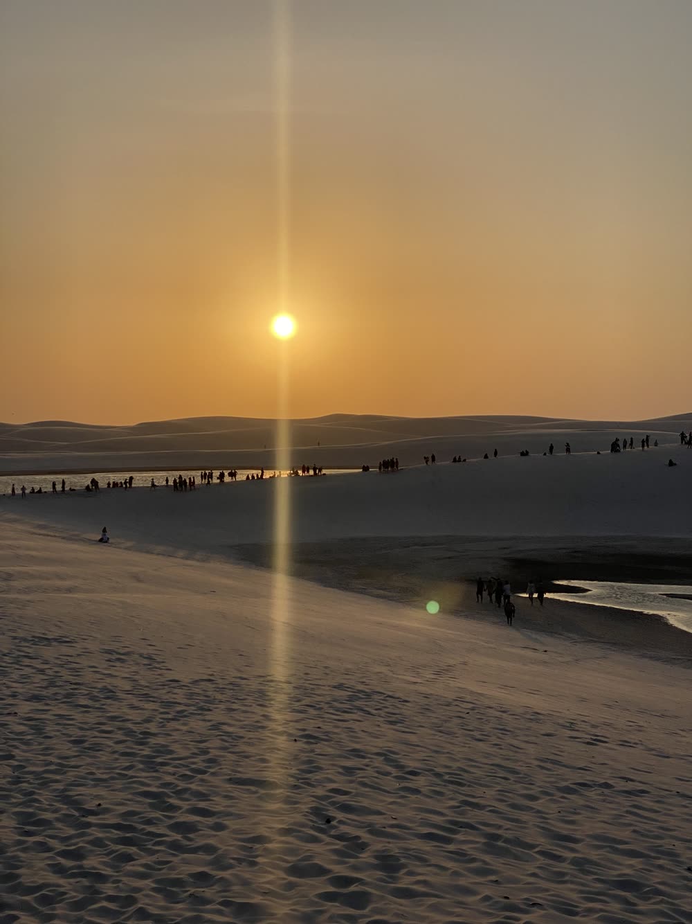 Pôr do sol sobre as dunas com pessoas assistindo do alto