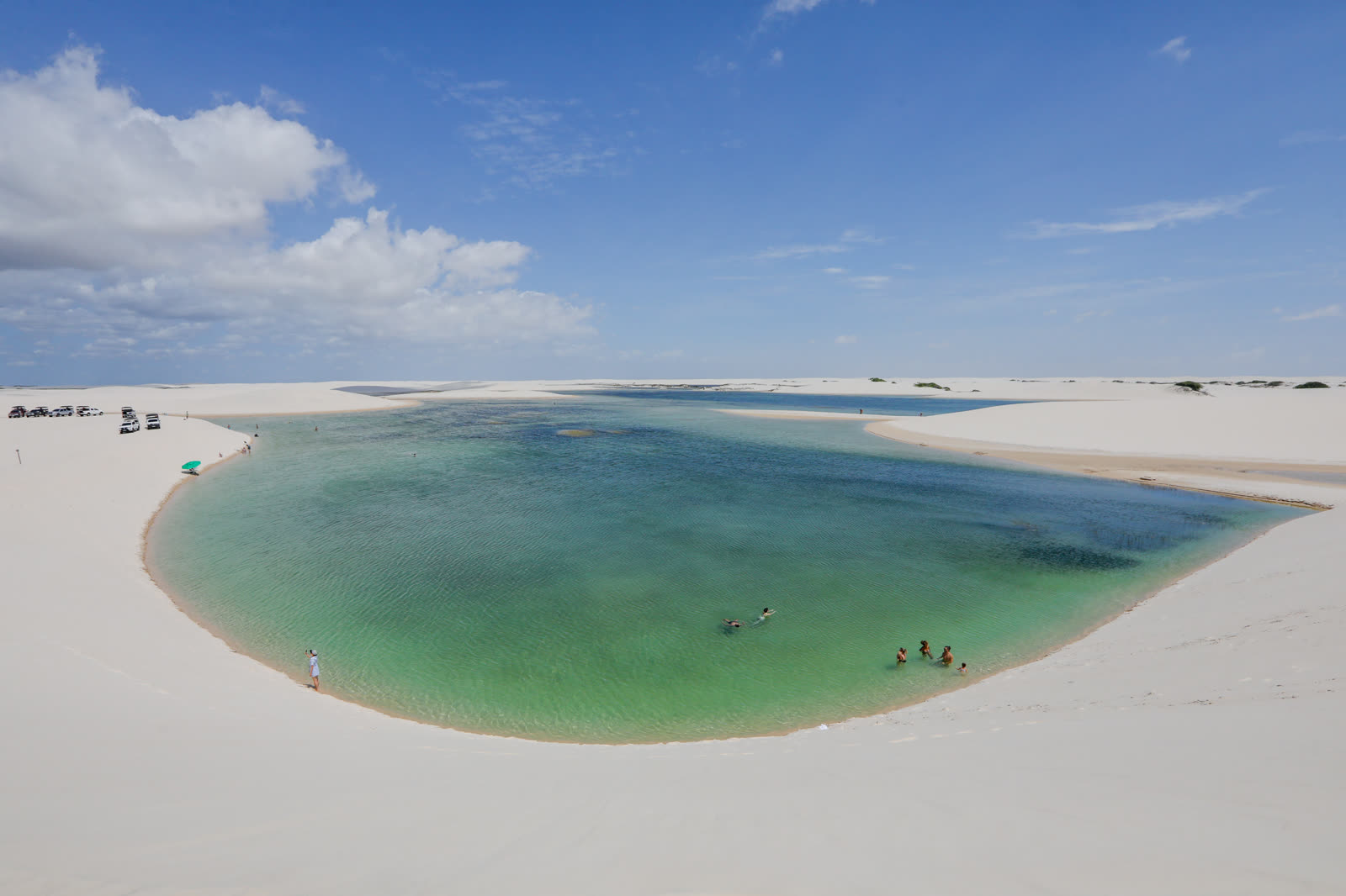Lagoa azul cercada de dunas brancas, com pessoas tomando banho